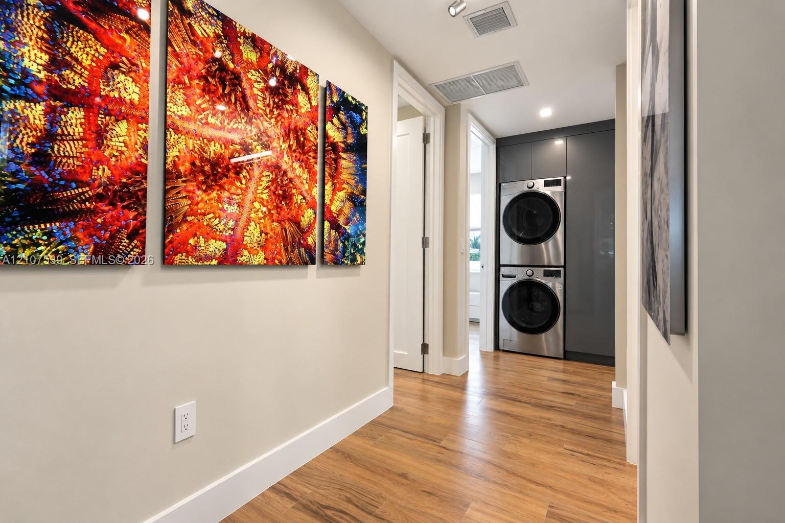 Laundry area featuring a stainless steel stacked washer and dryer unit, floor-to-ceiling charcoal gray cabinetry, and wood-finish flooring