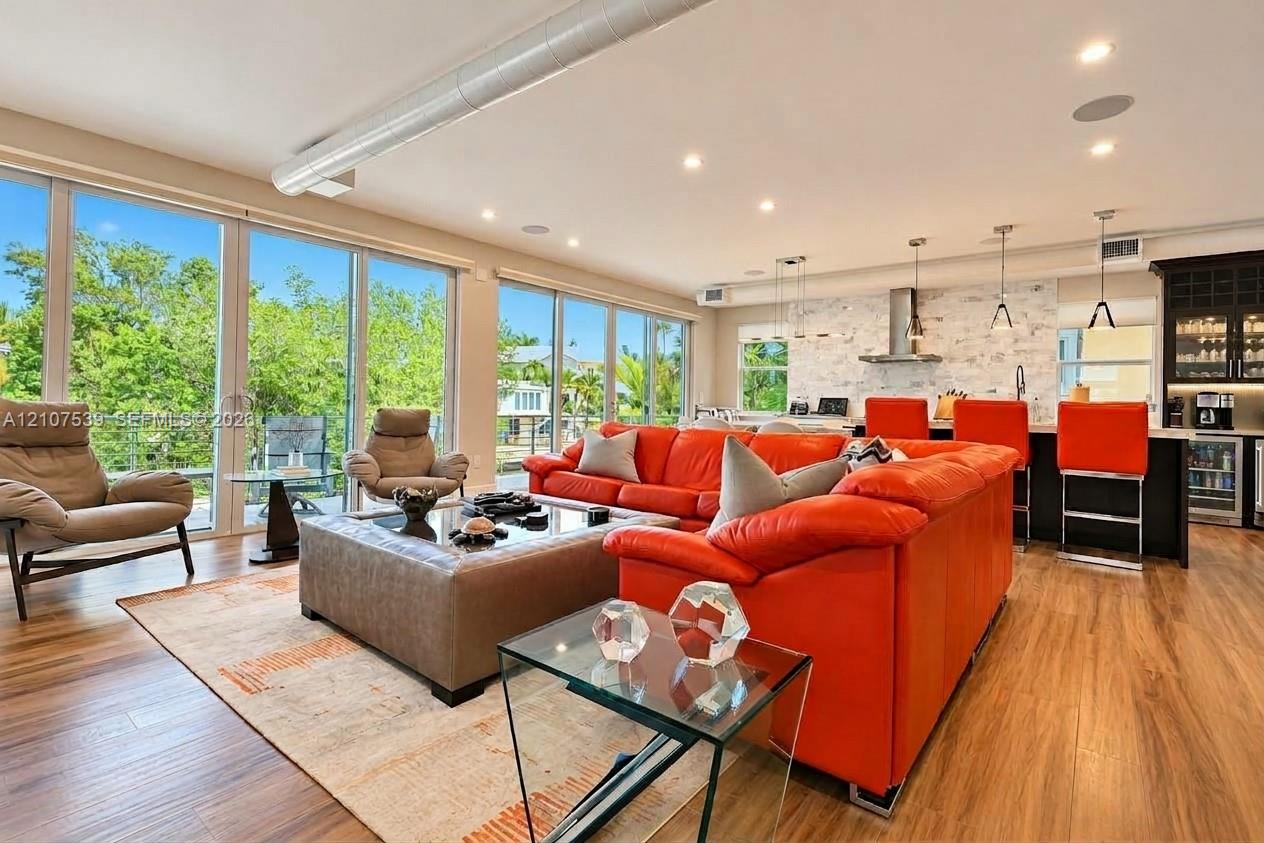 Open-concept interior featuring wood-finish flooring, floor-to-ceiling glass sliding doors, recessed lighting, exposed industrial-style ductwork, and a stone-tiled backsplash in the kitchen