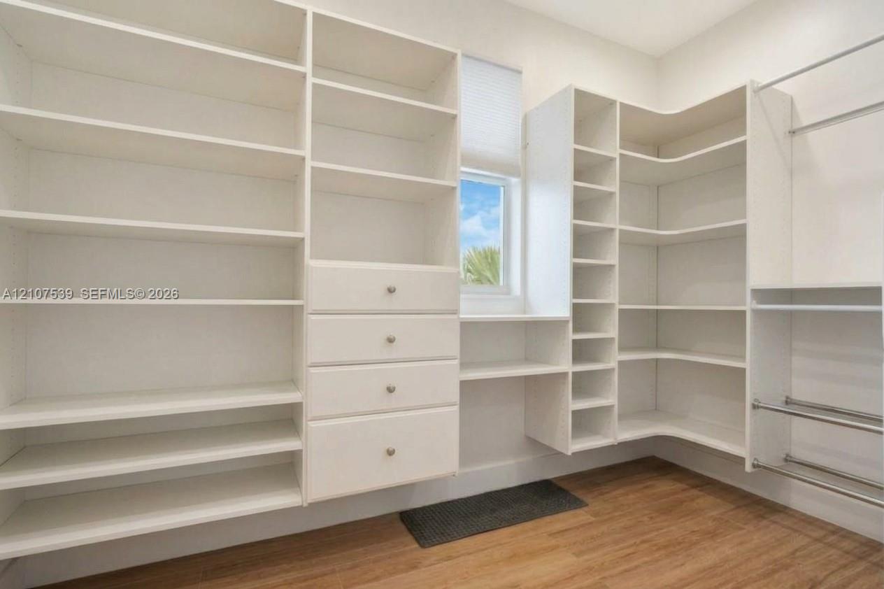 Custom white built-in shelving featuring floor-to-ceiling storage, integrated drawer units with metallic hardware, corner shelving, and metal hanging rods over wood-finish flooring