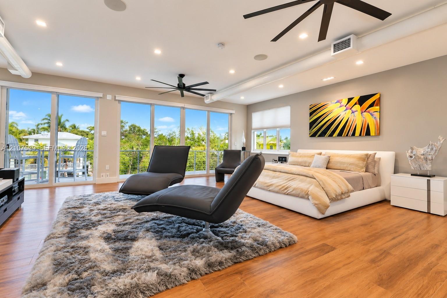 Open-concept interior featuring wood-finish flooring, floor-to-ceiling glass sliding doors, recessed lighting, matte black ceiling fans, and exposed ductwork