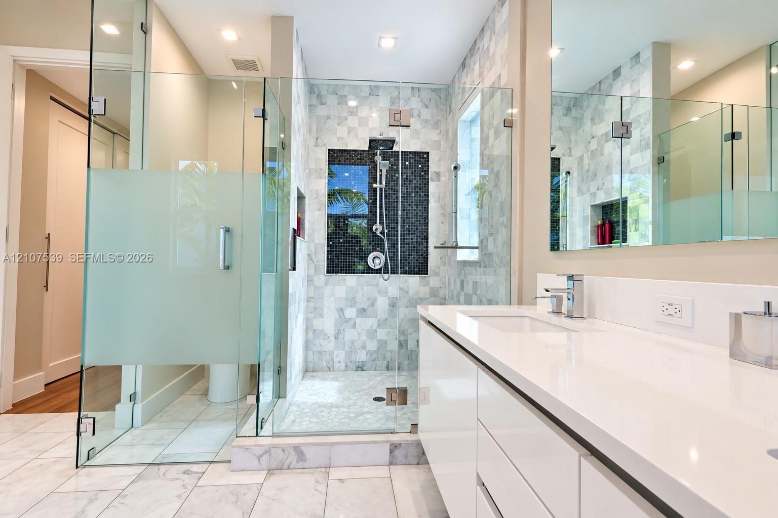 Bathroom featuring a white flat-panel vanity with a stone countertop, a glass-enclosed walk-in shower with tiled walls and a built-in recessed niche, and polished stone flooring