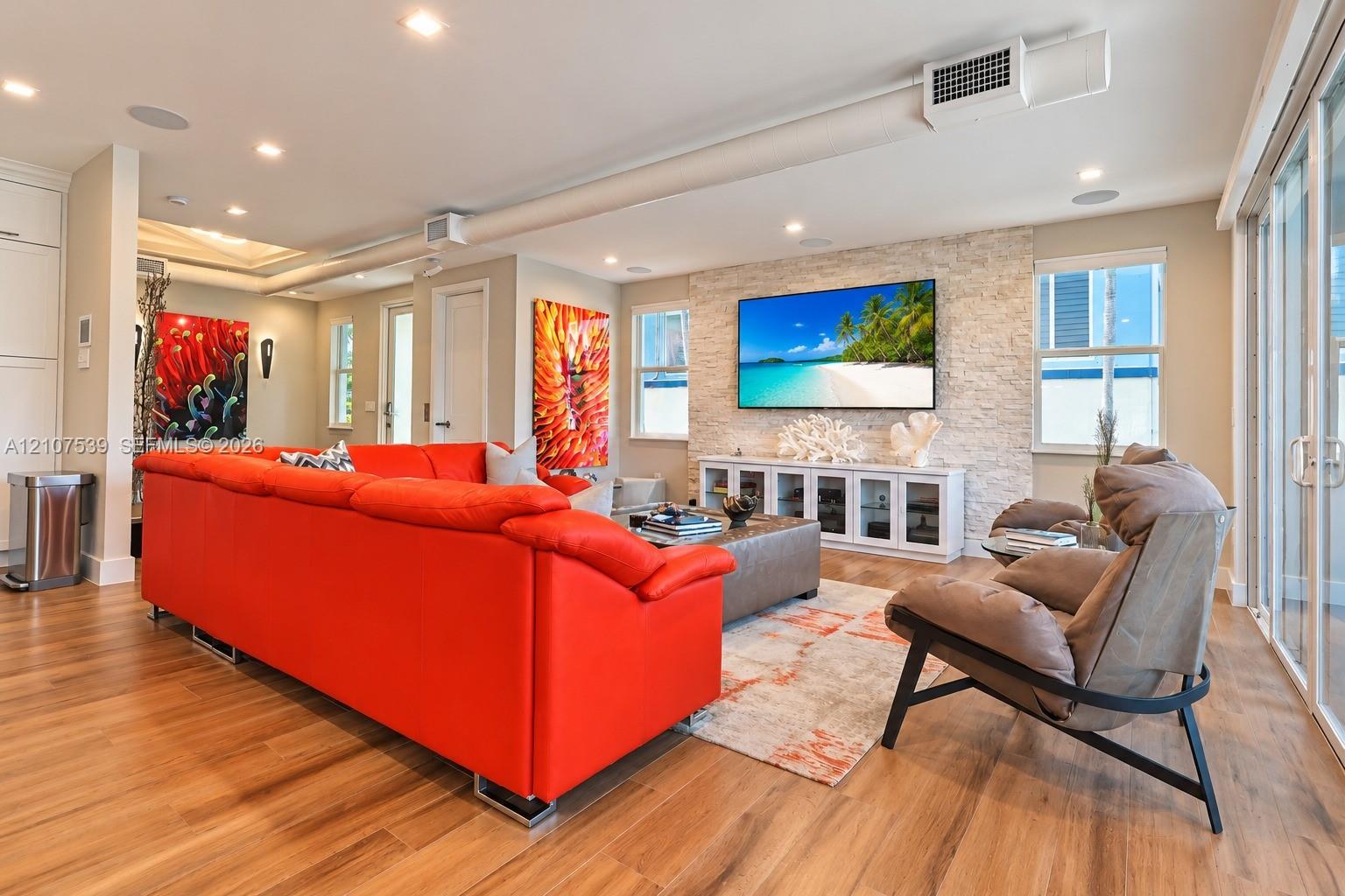 Living area featuring recessed lighting, wood-finish flooring, a textured stone accent wall, and glass sliding doors