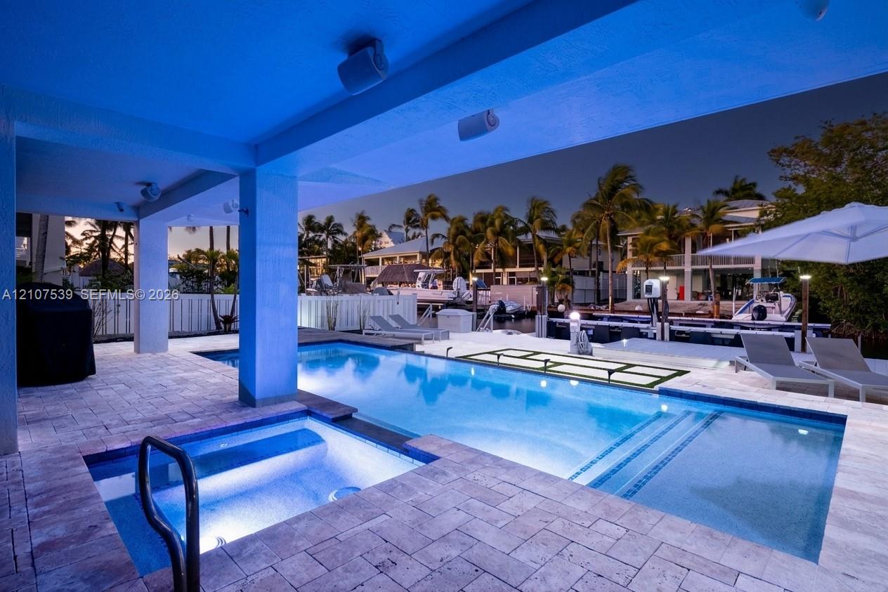 Covered outdoor patio featuring stone paver decking, an integrated spa, a rectangular swimming pool, and direct canal access