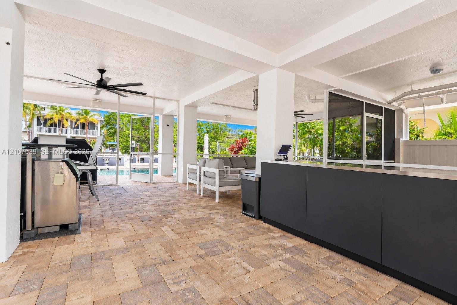 Covered patio featuring paver flooring, an outdoor kitchen with matte dark cabinetry, a built-in stainless steel grill, and a ceiling-mounted fan