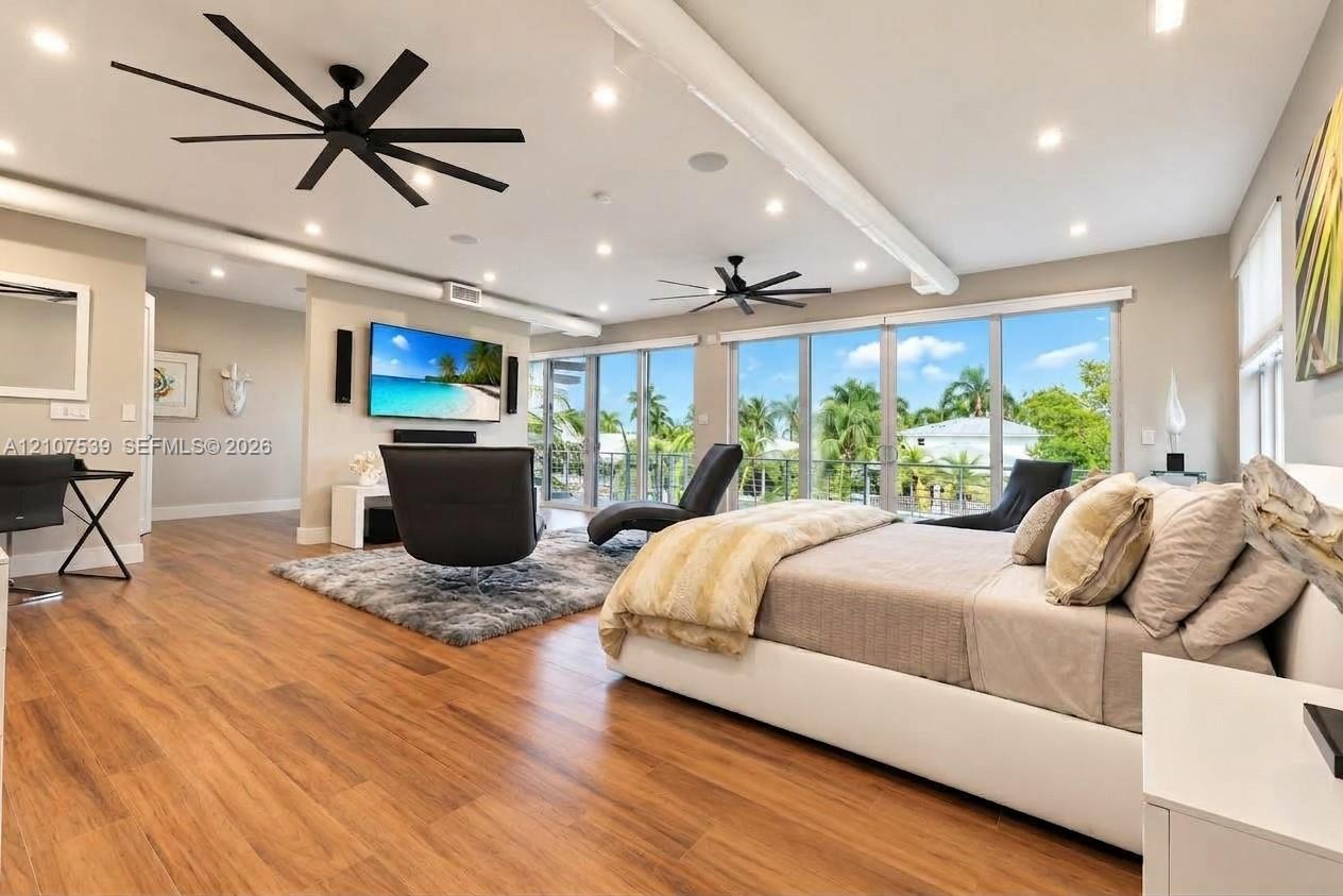 Wood-finish flooring, floor-to-ceiling glass wall, recessed lighting, matte black multi-blade ceiling fans, and built-in wall-mounted television console