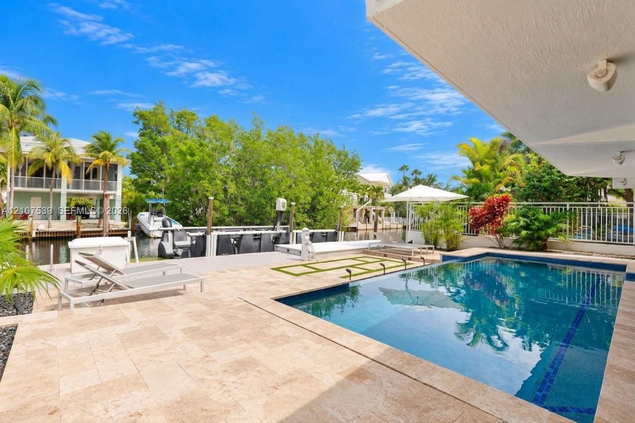 Waterfront pool deck featuring stone-finish pavers, integrated swimming pool, private boat dock, and canal frontage