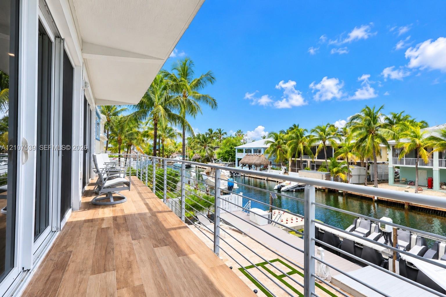 Covered balcony featuring wood-finish flooring, stainless steel cable railing, and sliding glass door access, overlooking a canal