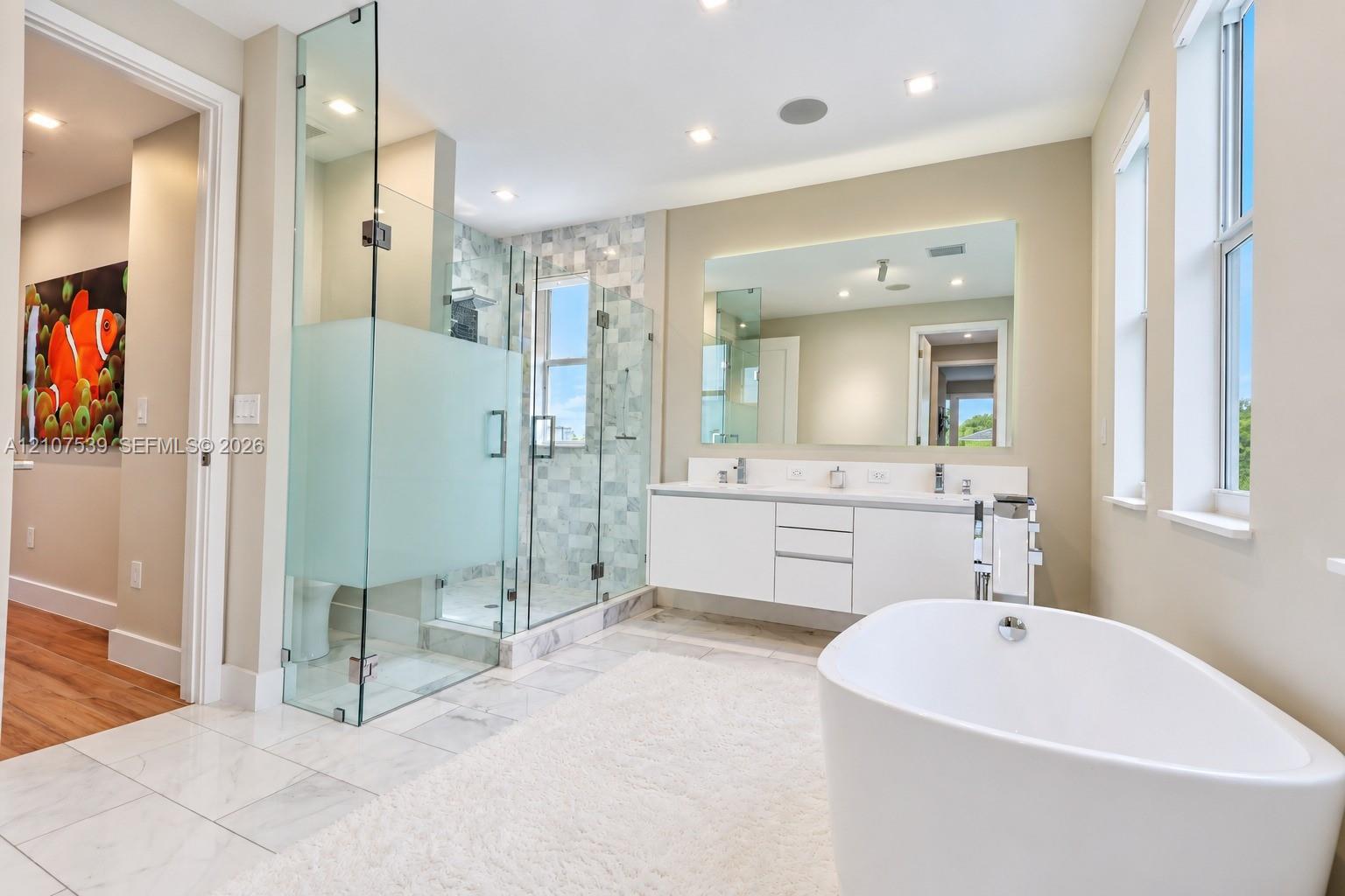 Freestanding soaking tub, glass-enclosed shower with tiled surround, and floating dual-sink vanity with a large wall-mounted mirror