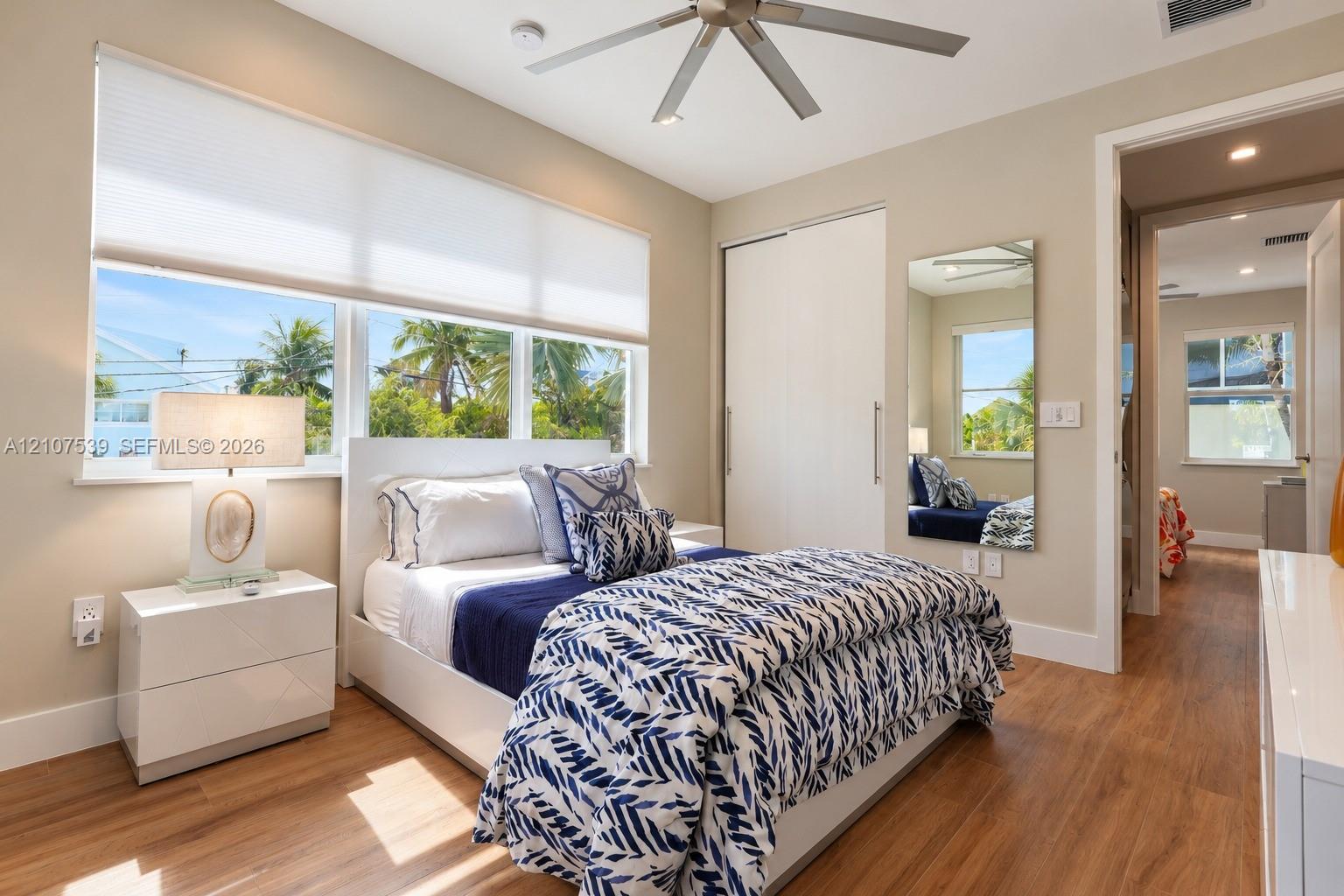 Wood-finish flooring, large windows with neutral roller shades, ceiling fan with light fixture, and built-in closet with sliding doors