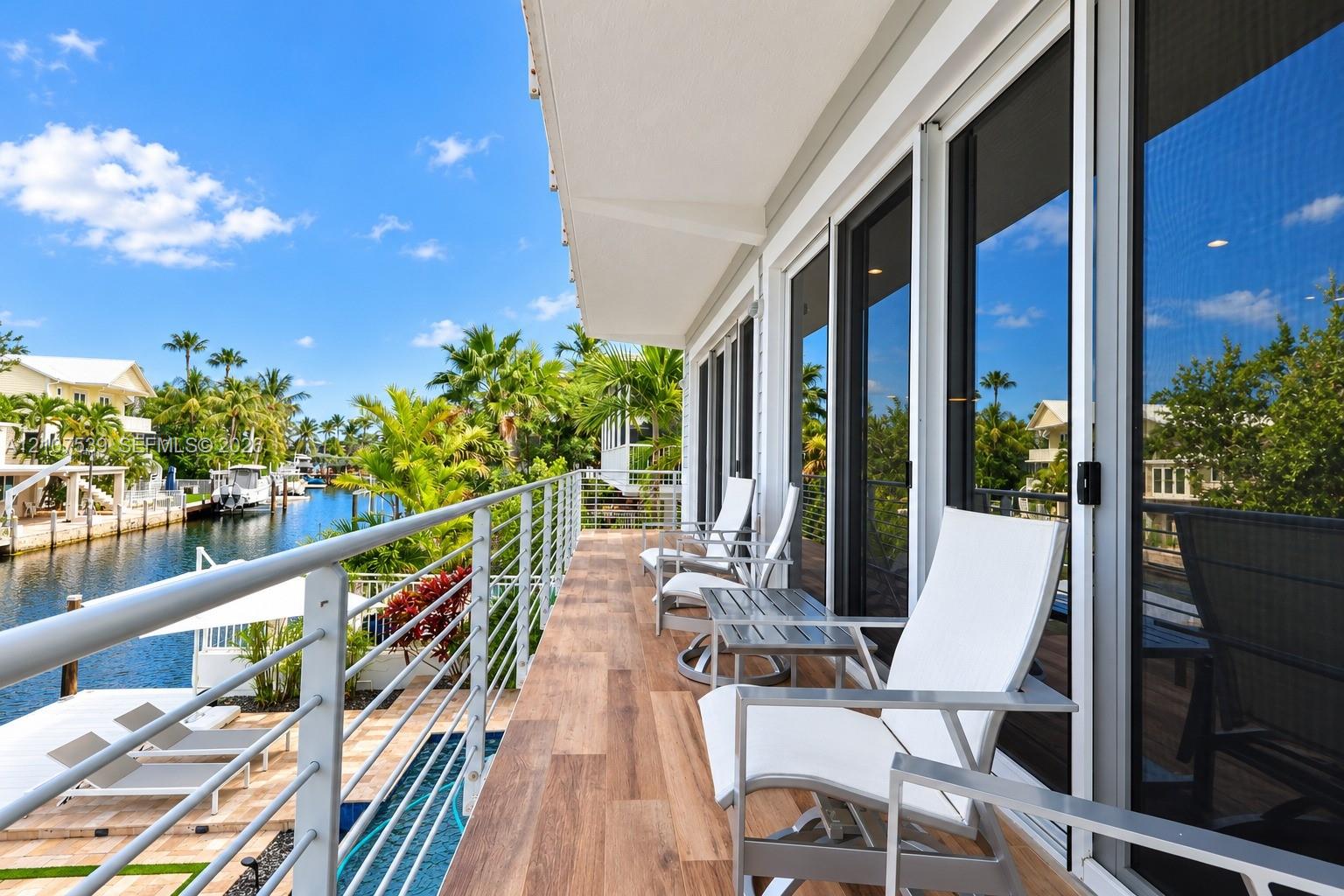 Waterfront balcony featuring wood-finish flooring, a horizontal cable railing system, and multiple floor-to-ceiling glass sliding doors
