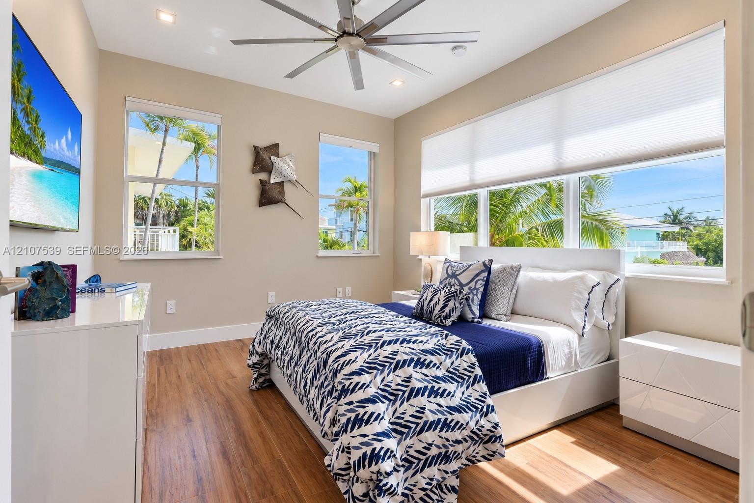 Room featuring wood-finish flooring, a multi-blade ceiling fan, recessed lighting, and large windows with integrated shades