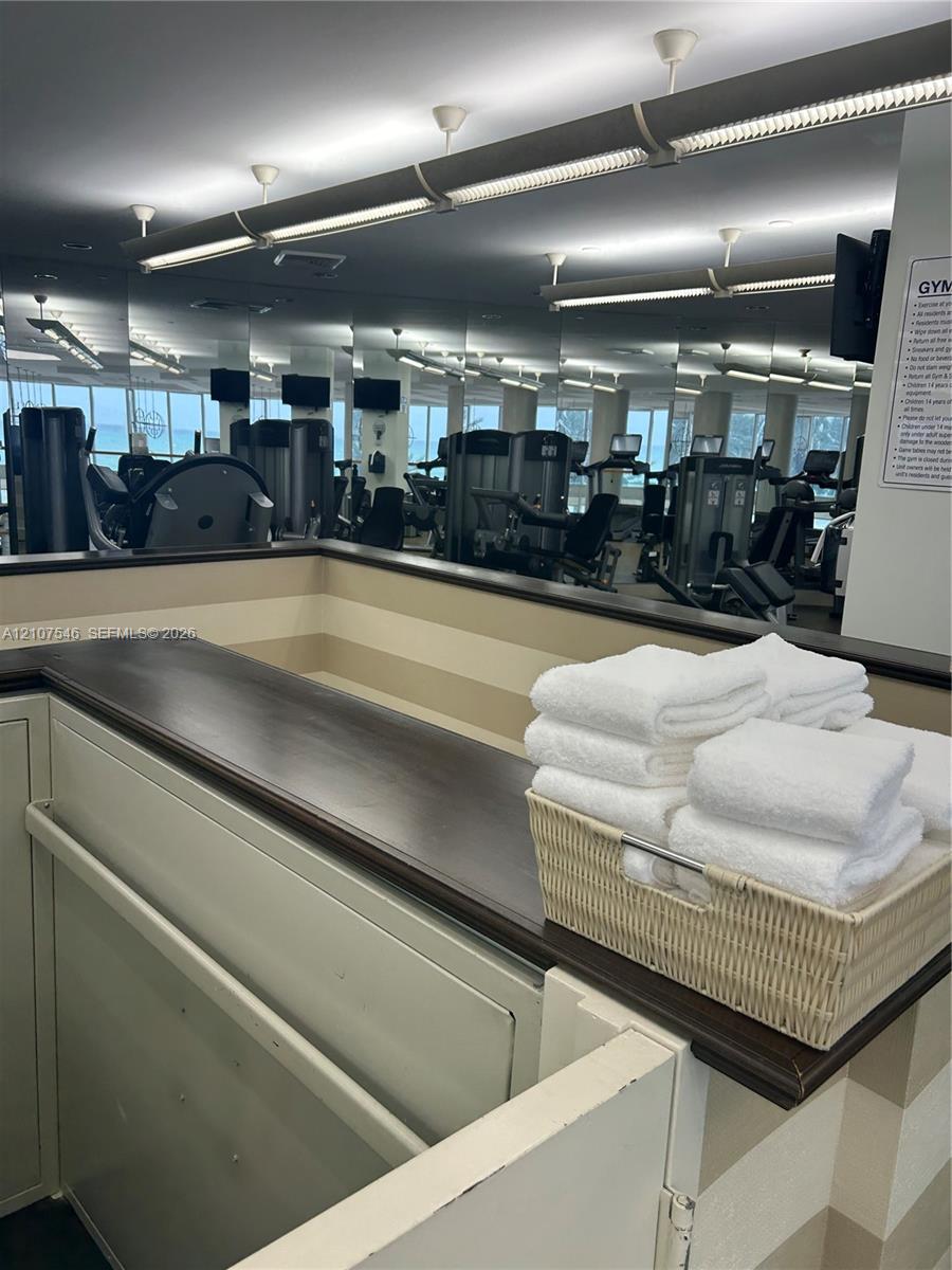 Fitness area featuring full-wall mirrors, recessed lighting, and a built-in service counter with a dark wood-finish top