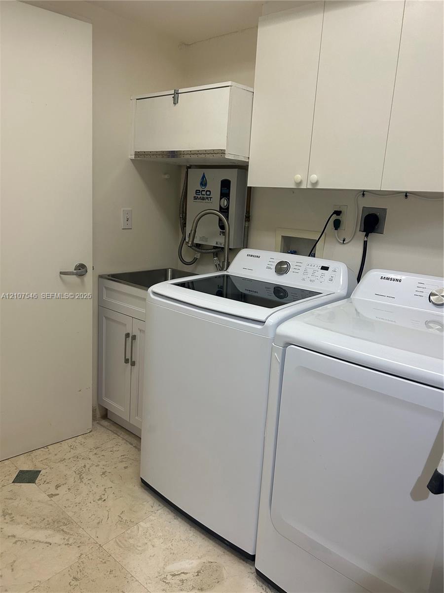 Utility area featuring white shaker-style cabinetry, wall-mounted storage units, a stainless steel sink with a high-arc pull-down faucet, and stone flooring