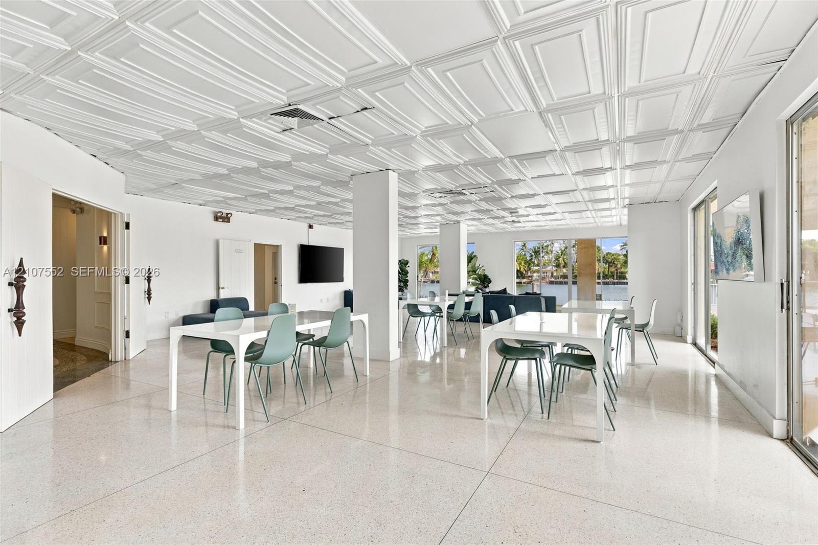 Expansive open-concept room featuring decorative coffered ceiling panels, polished stone flooring, and floor-to-ceiling glass sliding doors