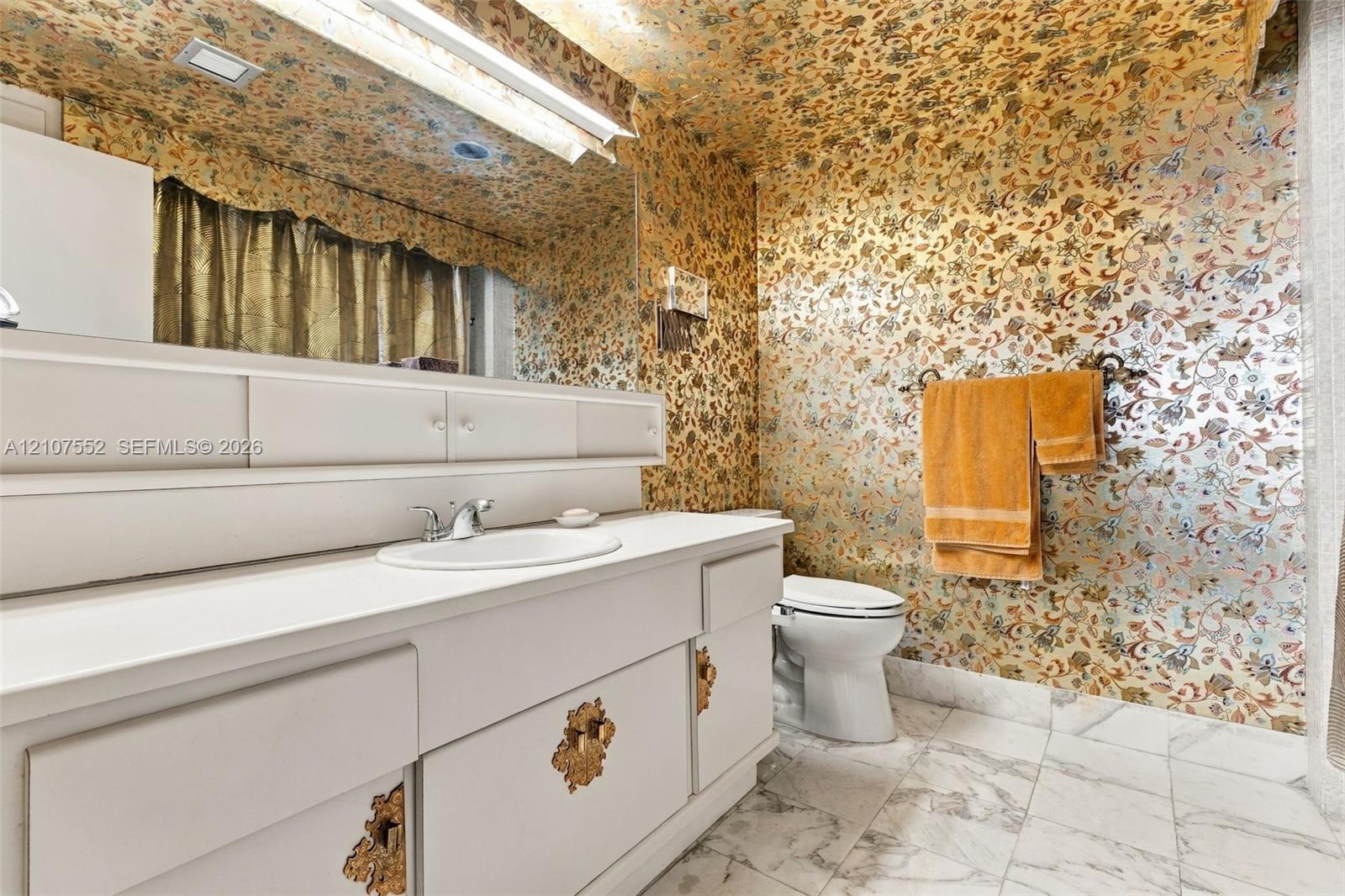 Bathroom featuring a white vanity with integrated cabinetry, an inset sink, a full-width wall mirror, and stone-finish tile flooring