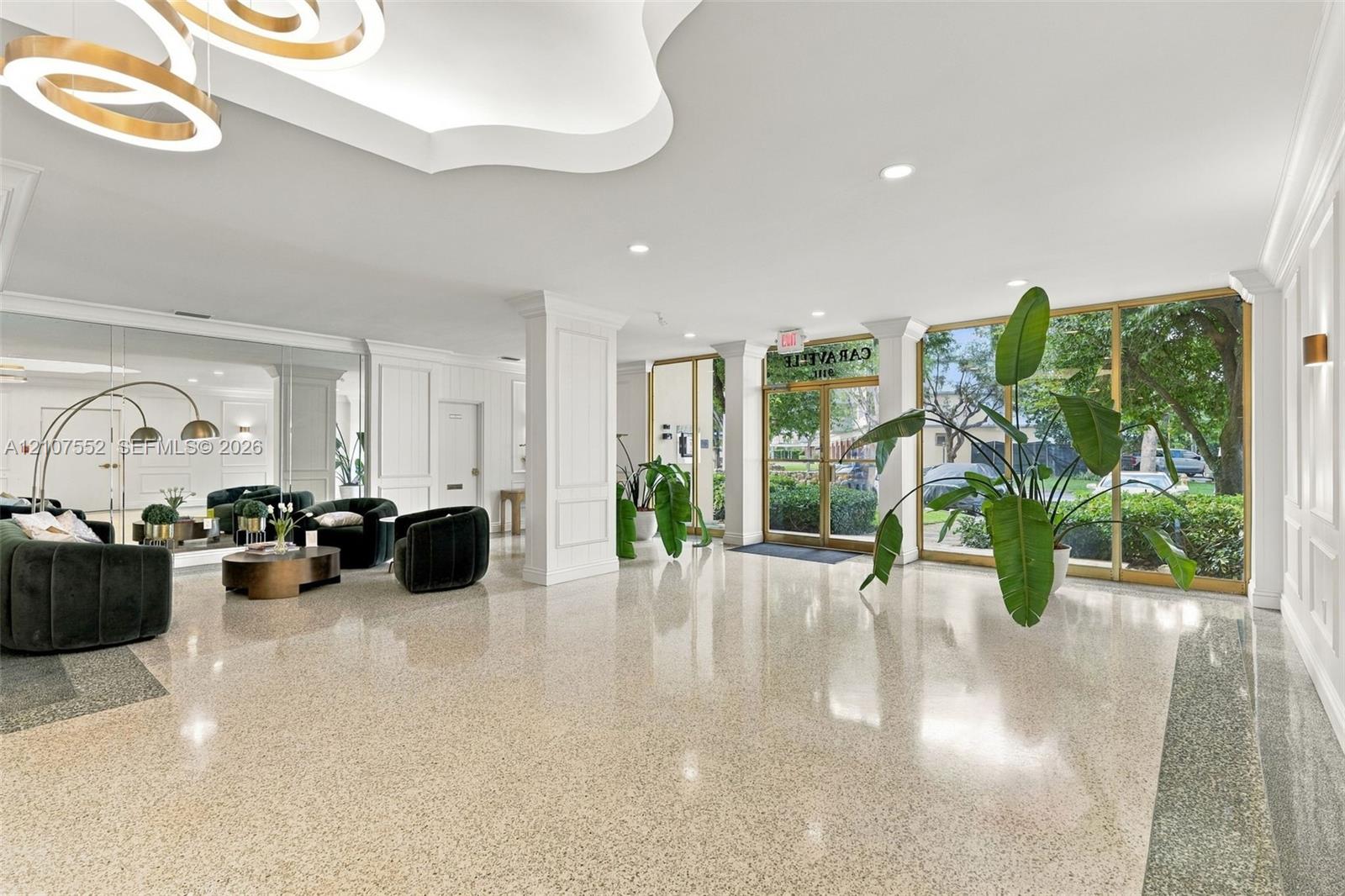 Spacious lobby featuring polished stone flooring, intricate crown molding, architectural columns, a modern multi-tiered chandelier, and floor-to-ceiling glass windows with metal framing