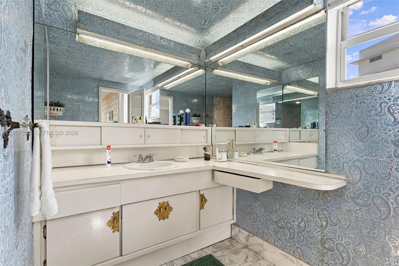 Built-in white vanity with integrated cabinetry, polished gold-toned hardware, solid-surface countertop, circular drop-in sink, and expansive wall-to-wall mirror