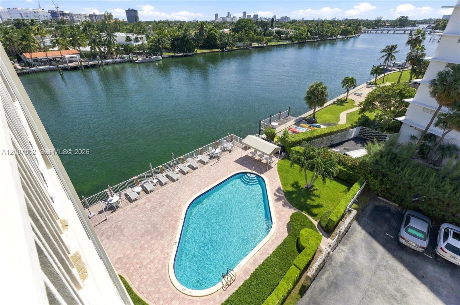 Waterfront swimming pool with paver patio, manicured landscaping, and bulkhead shoreline