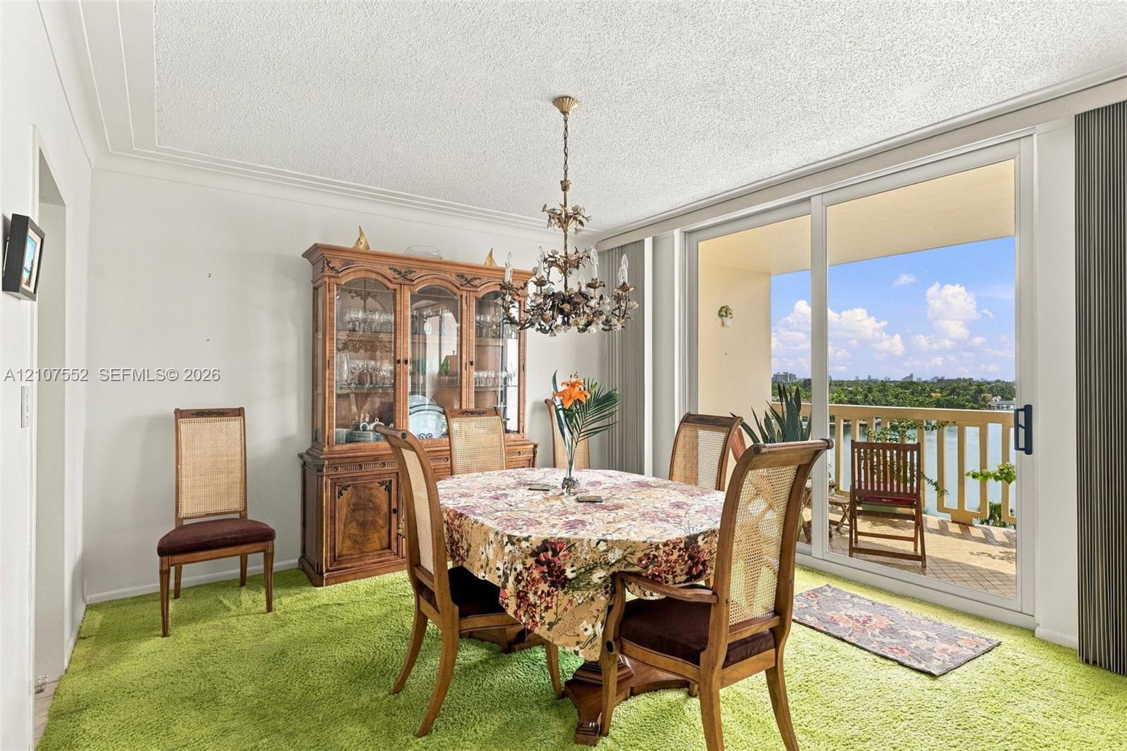 Dining area featuring a crystal chandelier and large glass sliding doors opening to an exterior balcony with water scenery