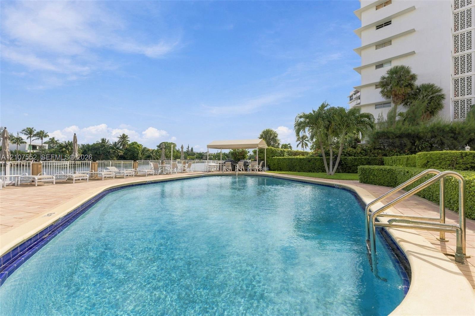 Swimming pool with tiled coping, metal handrail, paver pool deck, covered gazebo, and manicured hedge landscaping