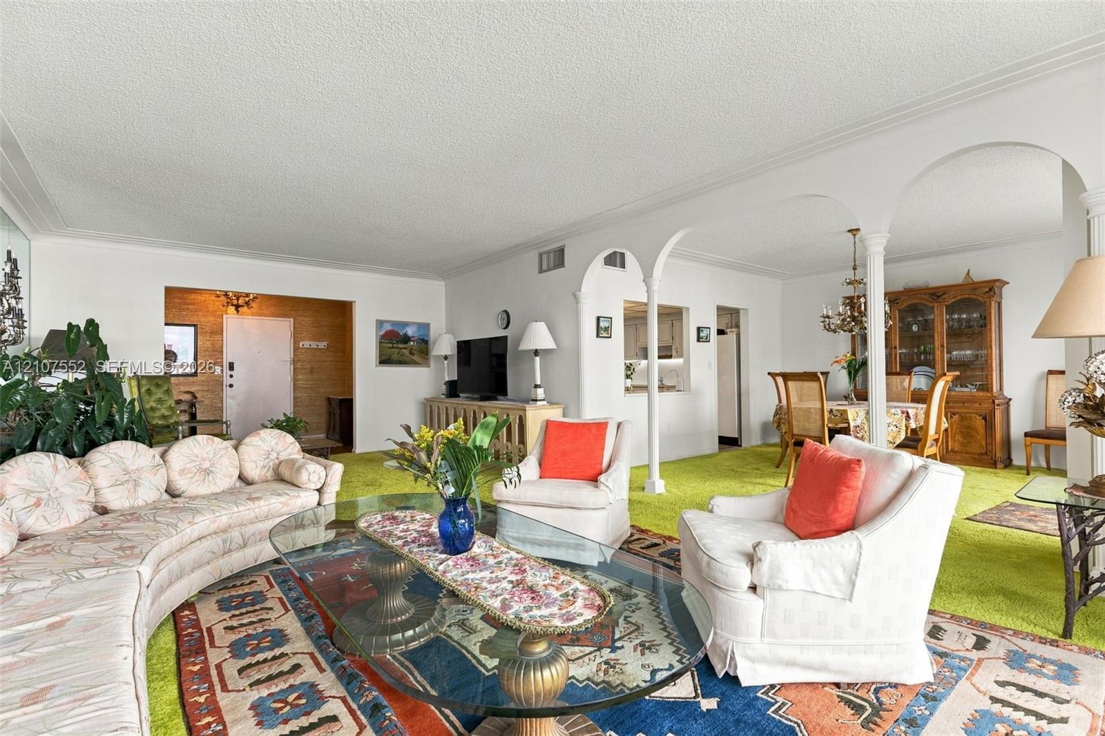 Living area featuring decorative archways with columns, a pass-through window to the kitchen, and a textured ceiling