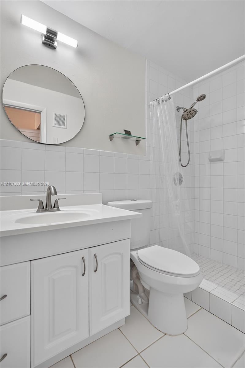 Bathroom featuring a vanity with integrated sink, circular wall-mounted mirror, modern light fixture, and tiled walk-in shower with adjustable handheld showerhead