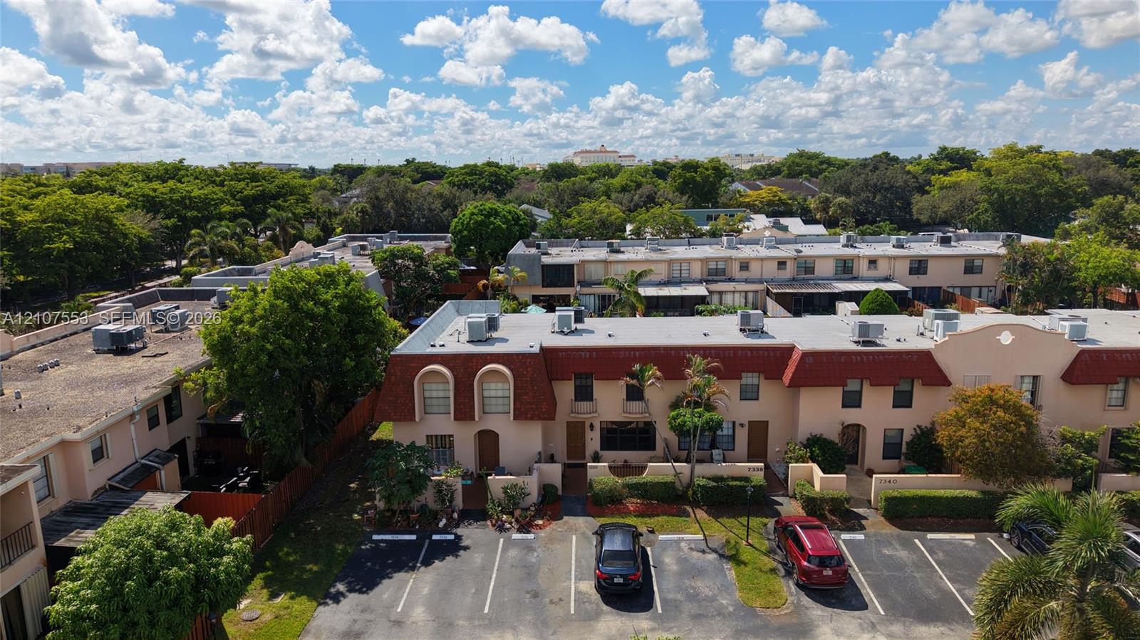 Multi-level townhome exterior featuring a red mansard roof, stucco facade, private enclosed entryway, dedicated surface parking, and mature landscaping