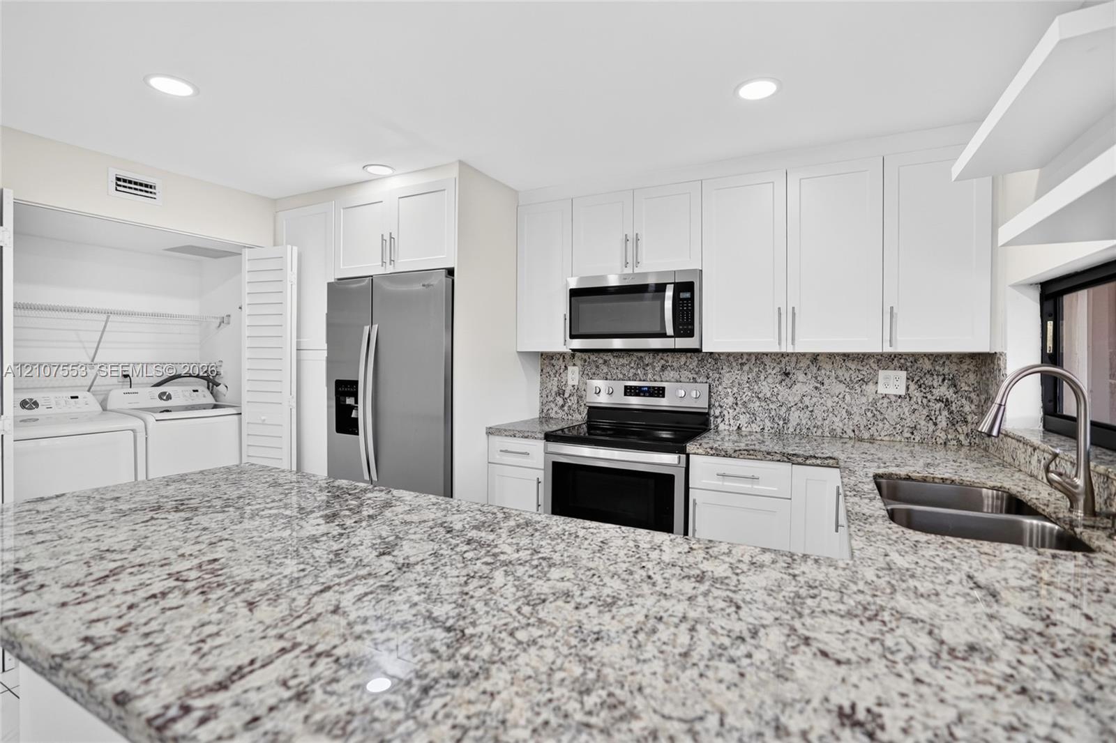 Kitchen featuring white shaker-style cabinetry, natural stone countertops, recessed lighting, stainless steel appliances, and a dual-basin undermount sink