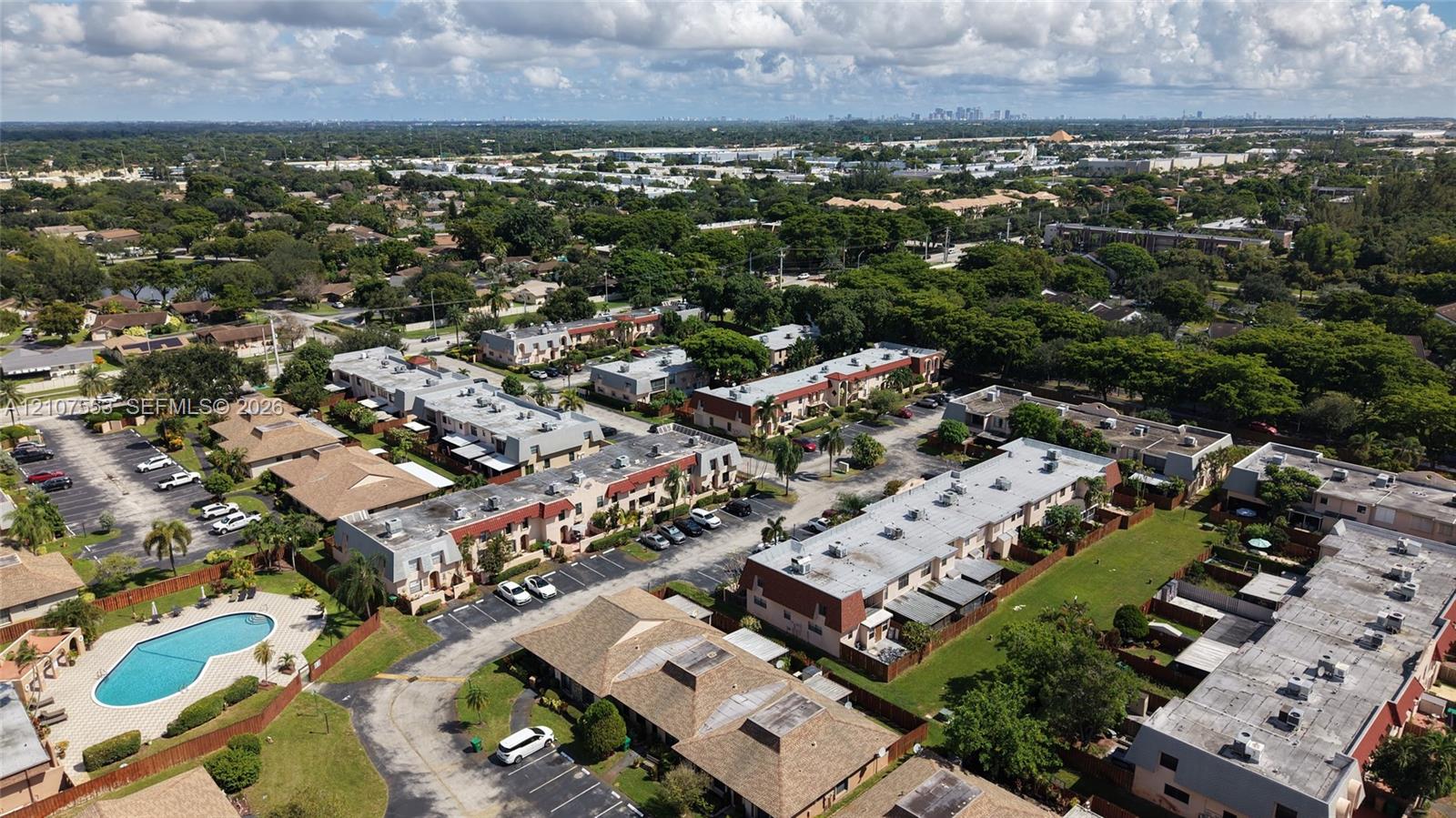 Aerial perspective featuring multi-story residential structures, paved surface parking lots, and a communal swimming pool set within landscaped grounds