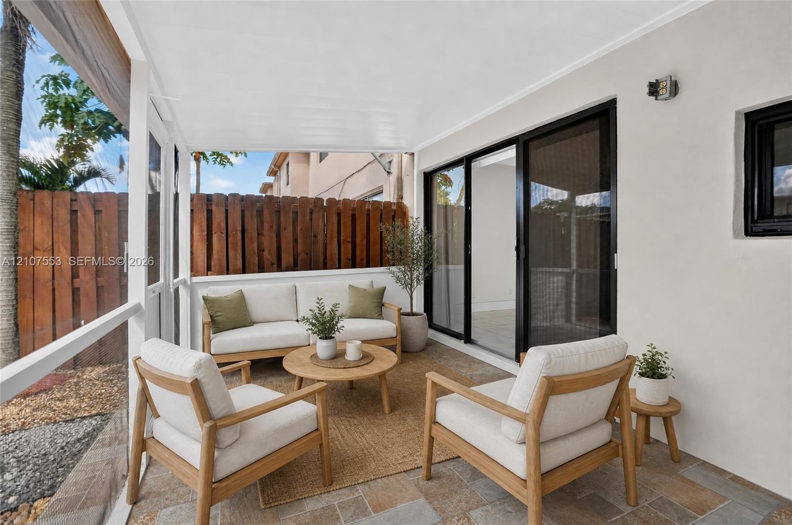 Screened-in patio featuring stone-tile flooring, a white-finished ceiling, and sliding glass doors with black frames, enclosed by a wood-plank privacy fence