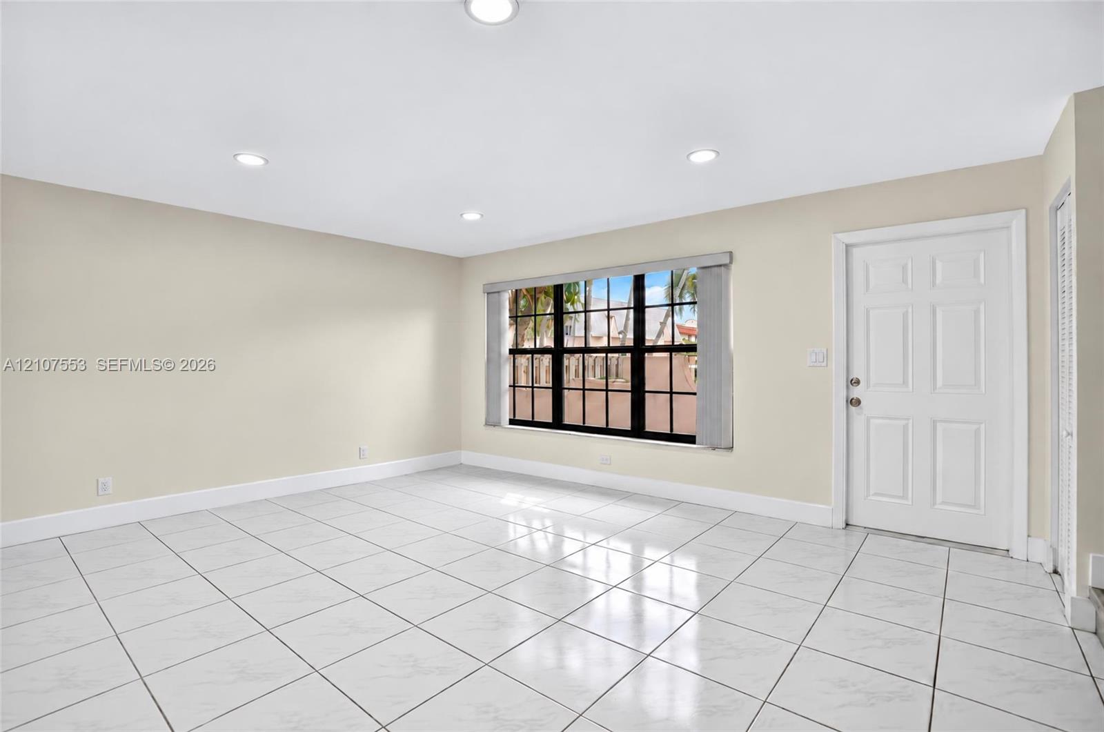 Neutral-toned interior featuring large-format tile flooring, recessed ceiling lighting, a six-panel exterior door, and a multi-pane window with a black frame