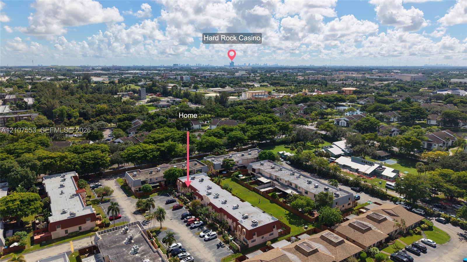 Aerial perspective of multi-family property featuring multi-story residential structures, paved parking areas, and abundant mature landscaping