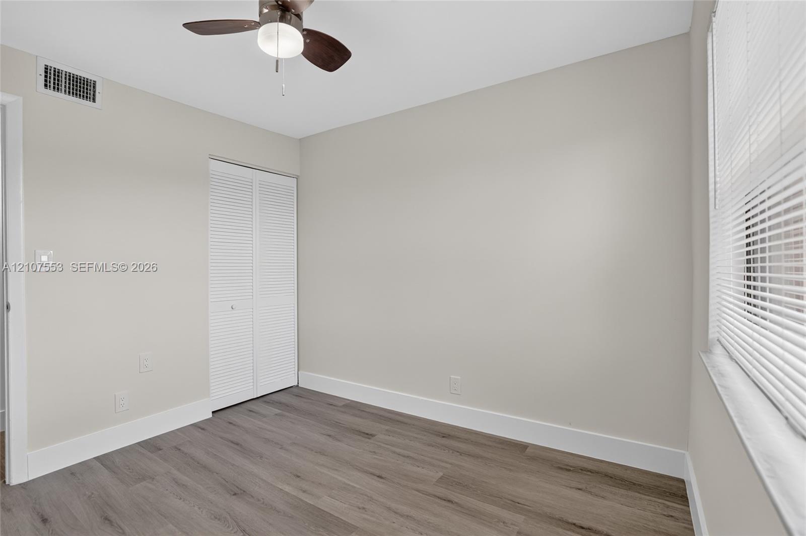 Neutral-toned room featuring wood-finish flooring, a ceiling fan with integrated lighting, and a bi-fold closet