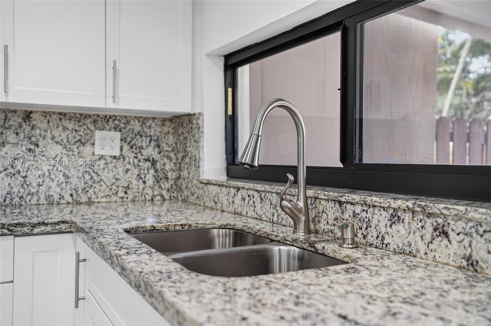 Stone-surface countertops with matching backsplash, white shaker-style cabinetry, stainless steel double-basin undermount sink, and high-arc pull-down faucet featuring a brushed metallic finish