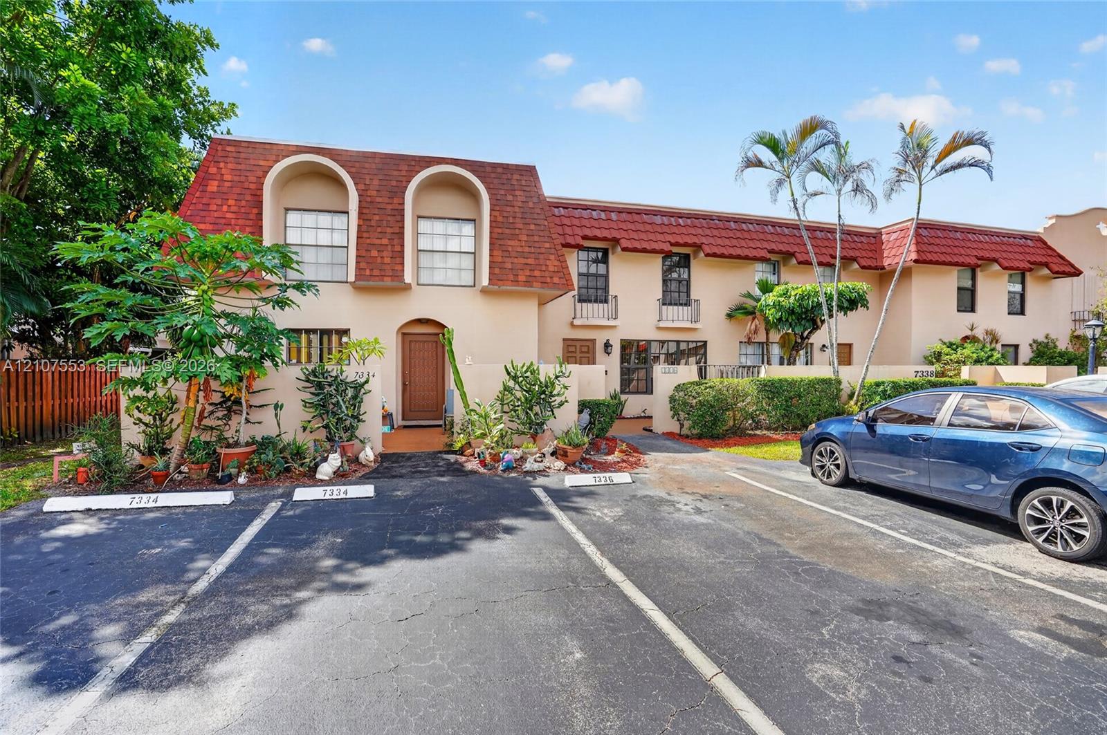 Two-story exterior featuring a mansard roof with shingle tiles, arched window detailing, stucco facade, and dedicated assigned parking spaces