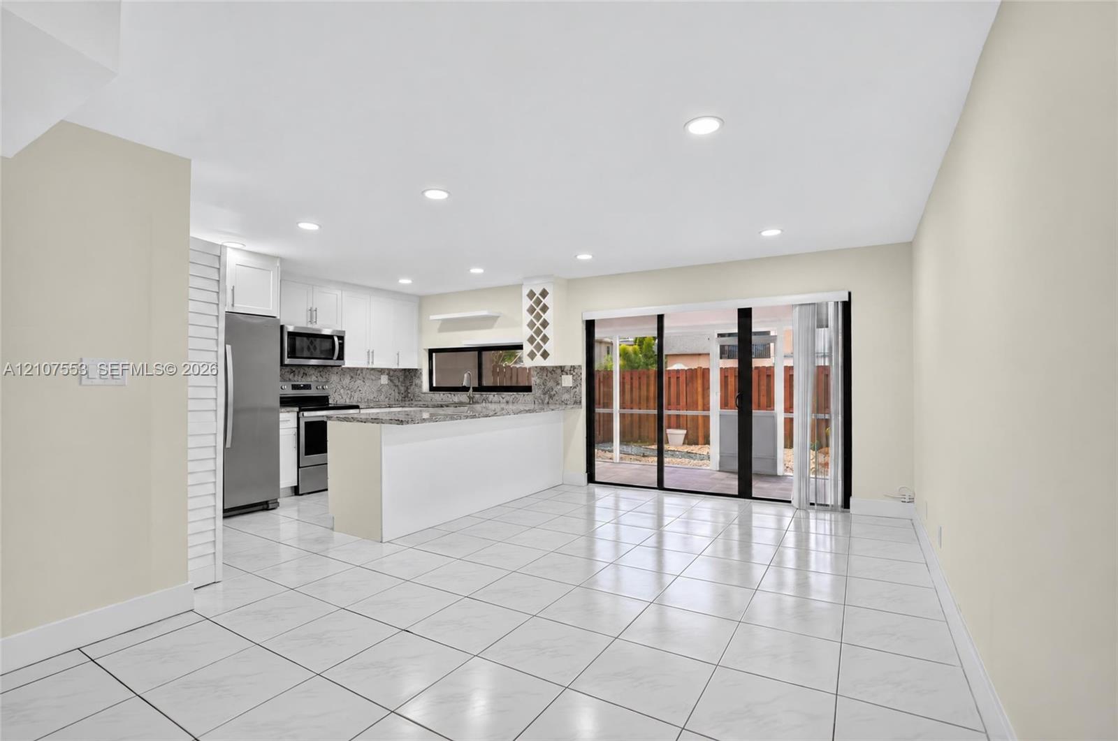 Open-concept kitchen featuring a breakfast bar, stone-finish countertops, stainless steel appliances, recessed lighting, and tile flooring