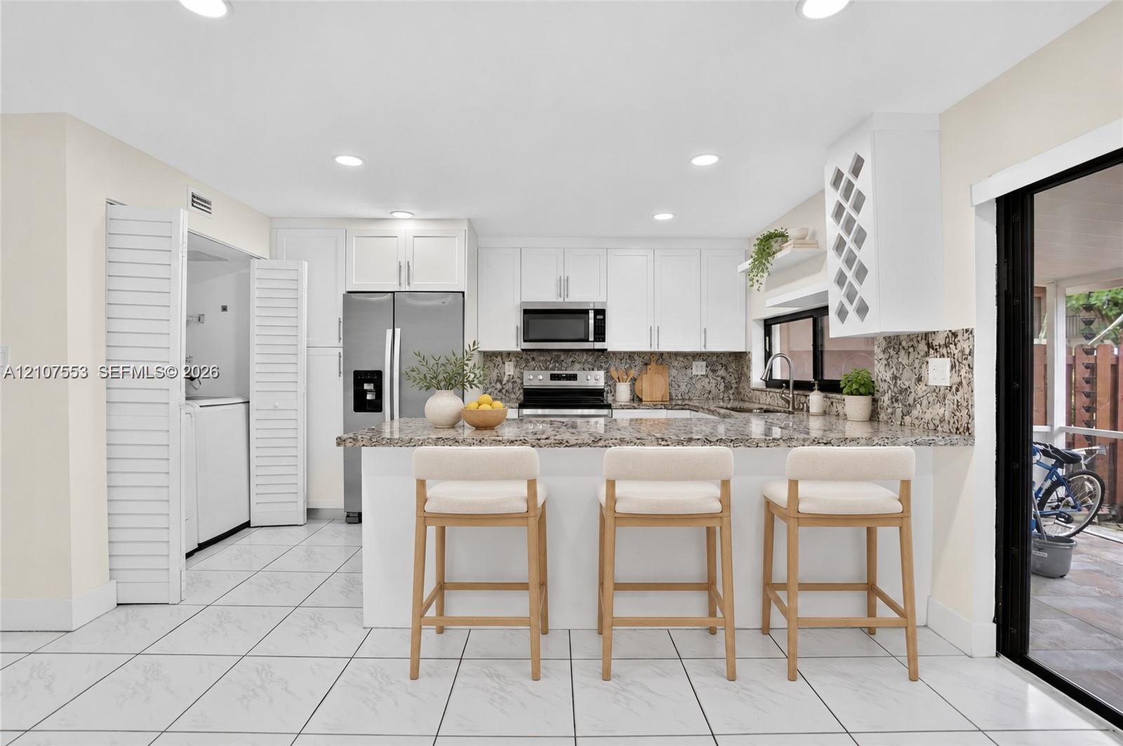 Kitchen featuring white shaker-style cabinetry, stone-finish countertops, stainless steel appliances, a built-in wine rack, and tile flooring