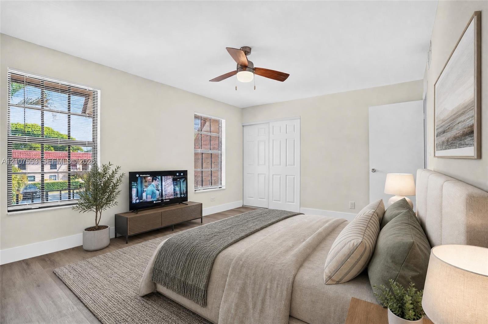 Bedroom featuring wood-finish flooring, dual windows, ceiling fan with integrated lighting, and a closet with paneled sliding doors