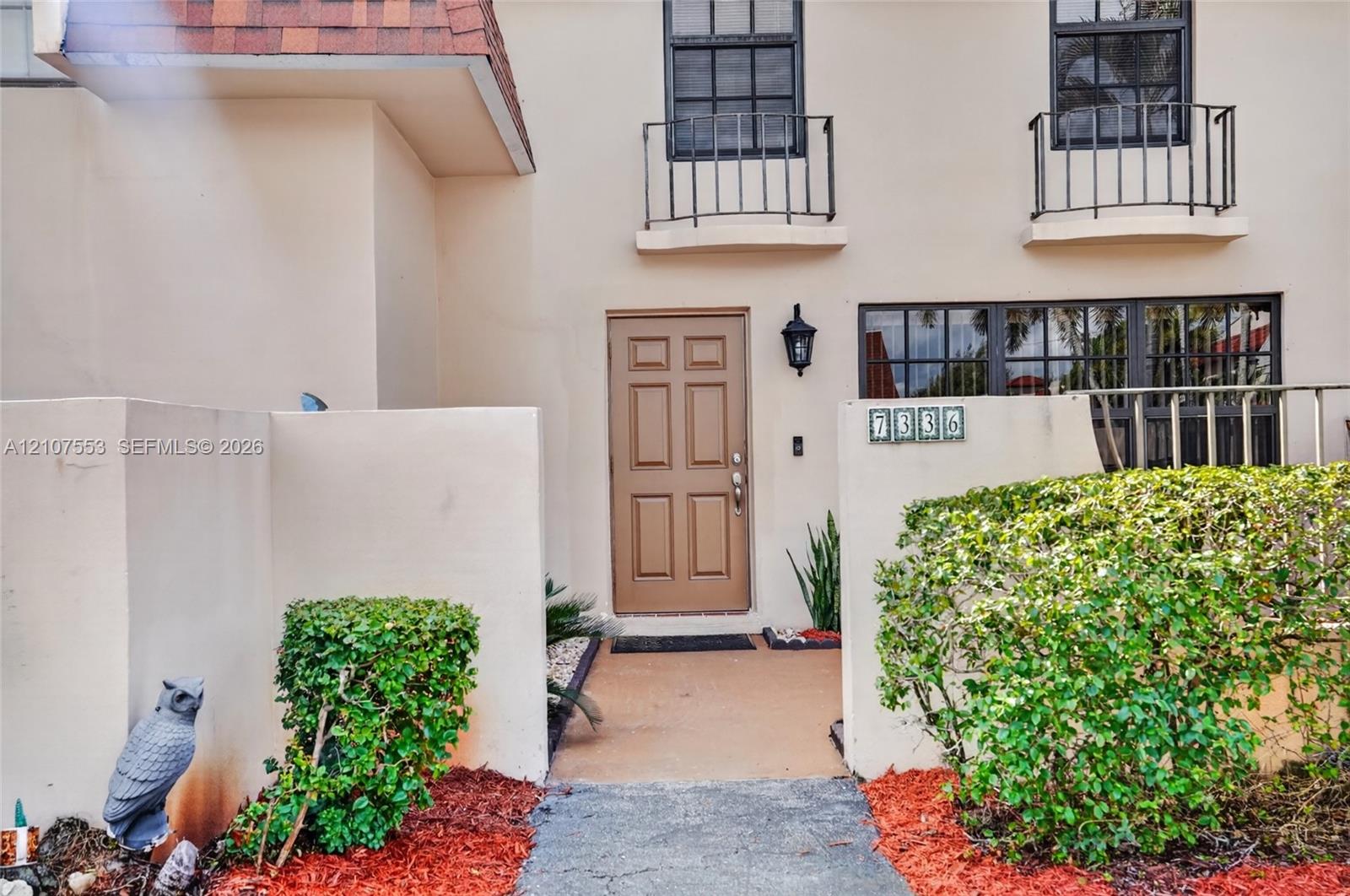 Stucco exterior featuring dual Juliet balconies, six-panel entry door, and a private enclosed front courtyard