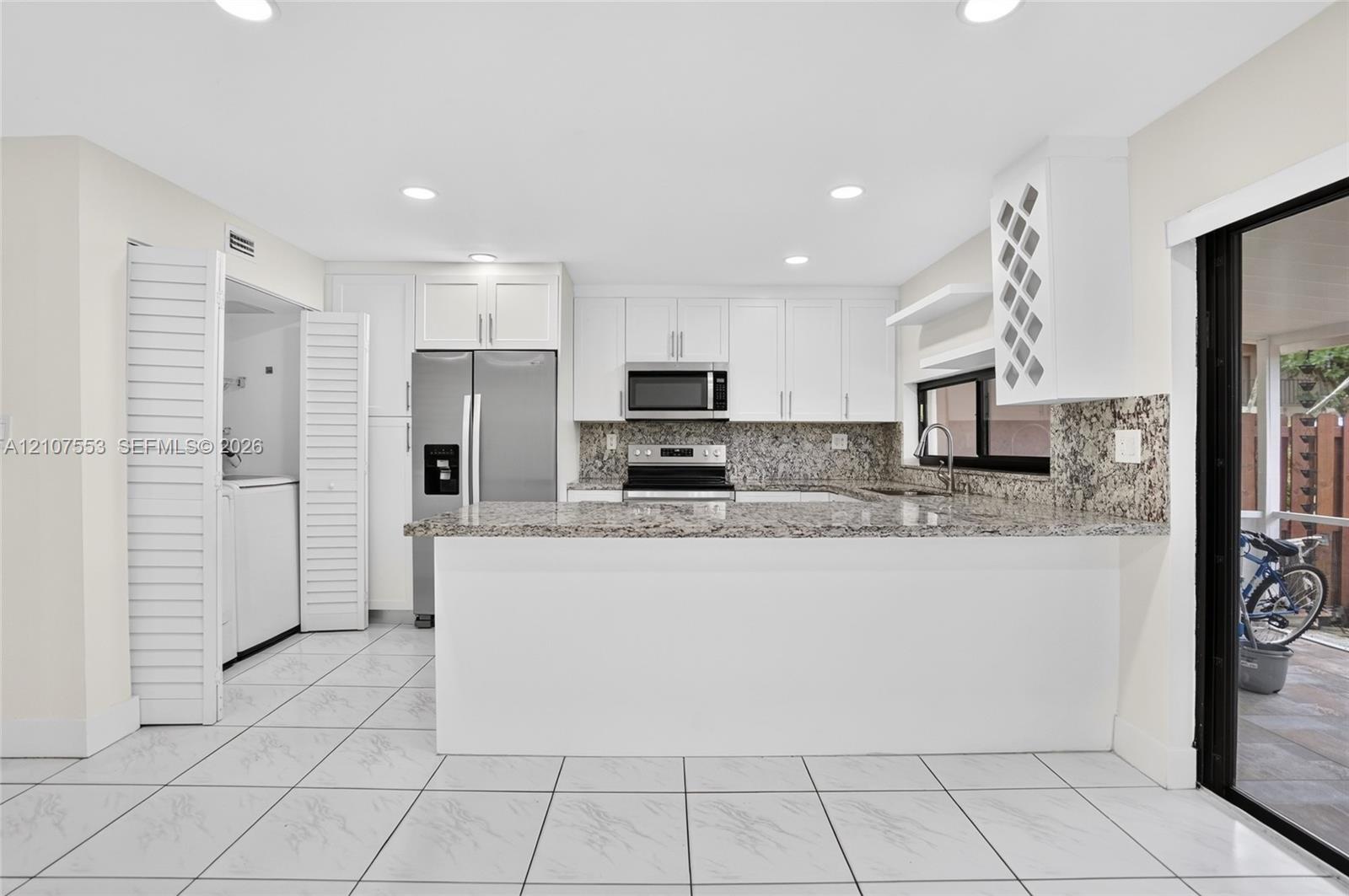 Kitchen featuring white cabinetry, stone countertops, stainless steel appliances, built-in wine storage, and ceramic tile flooring