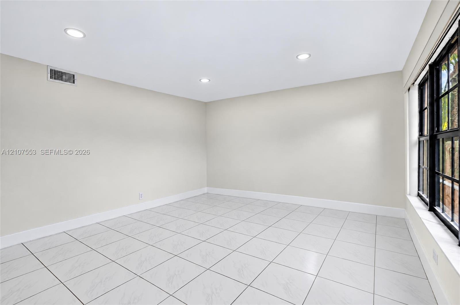 Neutral-toned interior space featuring light-colored tile flooring, recessed lighting, and a multi-pane window with a black frame