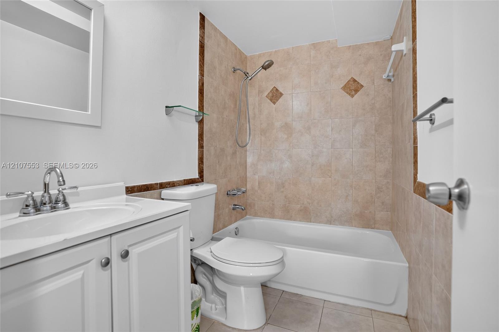 Bathroom featuring a white vanity cabinet, ceramic tile tub surround with decorative accents, wall-mounted mirror, and a combination bathtub and shower