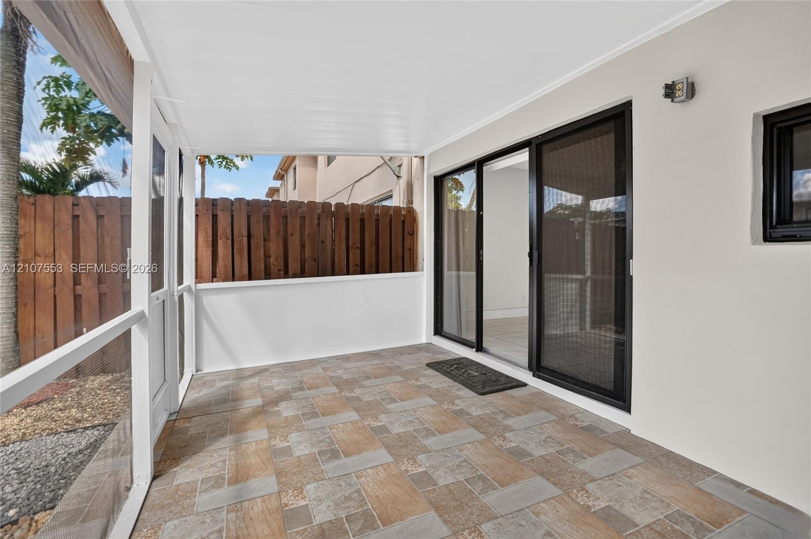 Screened-in patio featuring patterned tile flooring, a solid white ceiling, a white privacy enclosure, and a sliding glass door entry