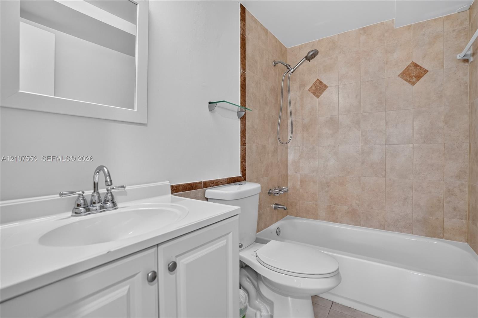 White vanity with integrated basin and polished metal faucet, complemented by a bathtub with a handheld shower head and tiled surround featuring decorative accents