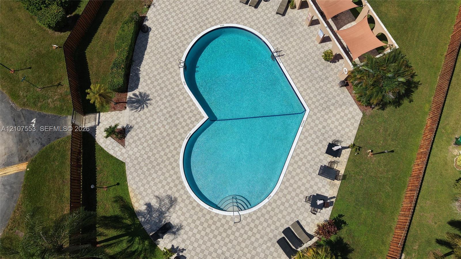 Heart-shaped swimming pool with built-in steps, surrounded by a paved patio, manicured lawn, and wooden perimeter fencing