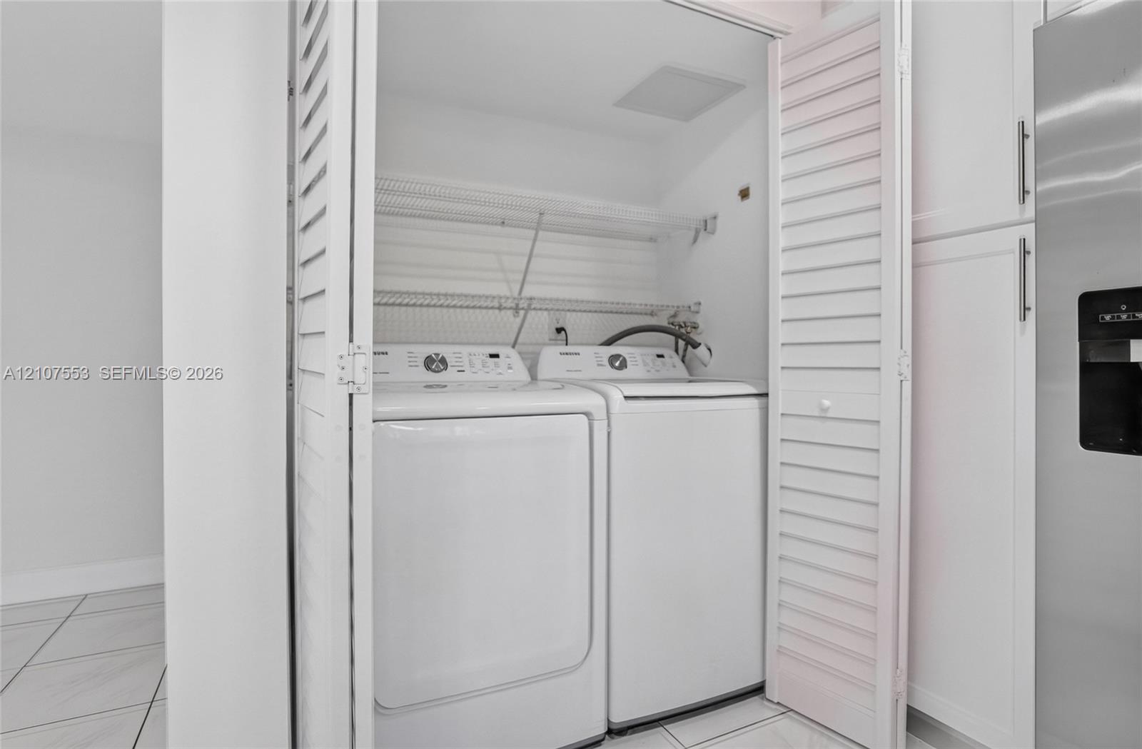 Laundry closet featuring white louvered doors, wire shelving, and tiled flooring