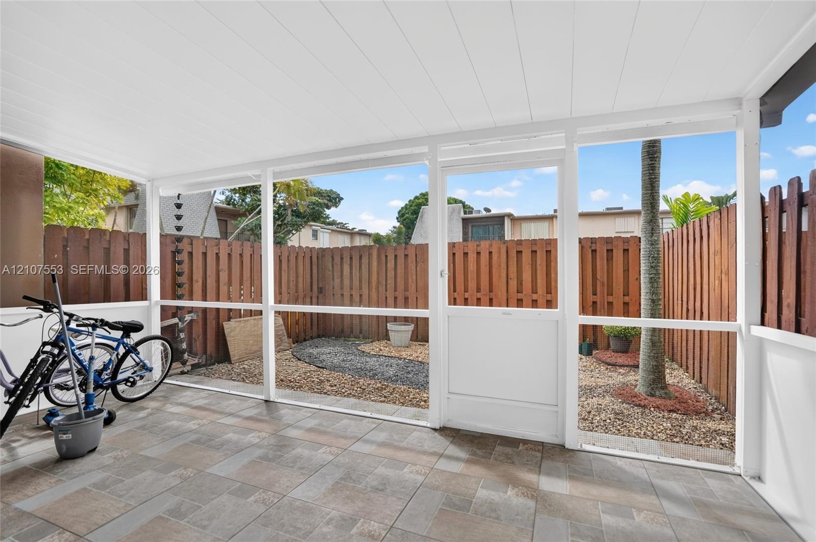 Screened-in patio with tile flooring, a white paneled ceiling, and a wooden privacy fence enclosing a gravel courtyard