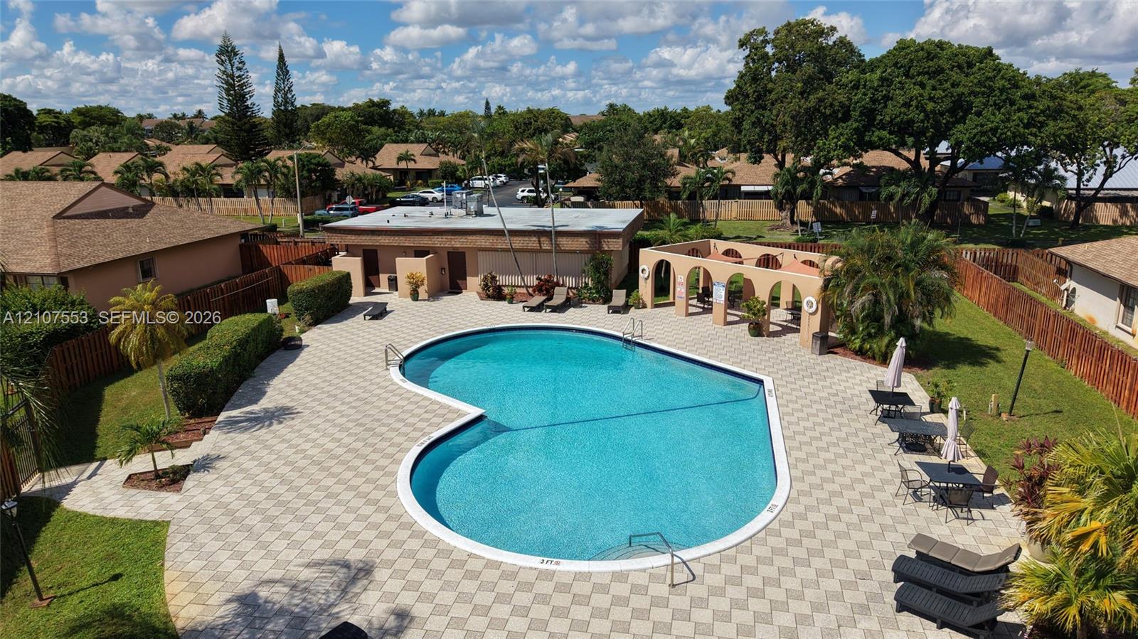 Community pool featuring an expansive paved deck, covered seating pavilion with arched masonry, and manicured green space