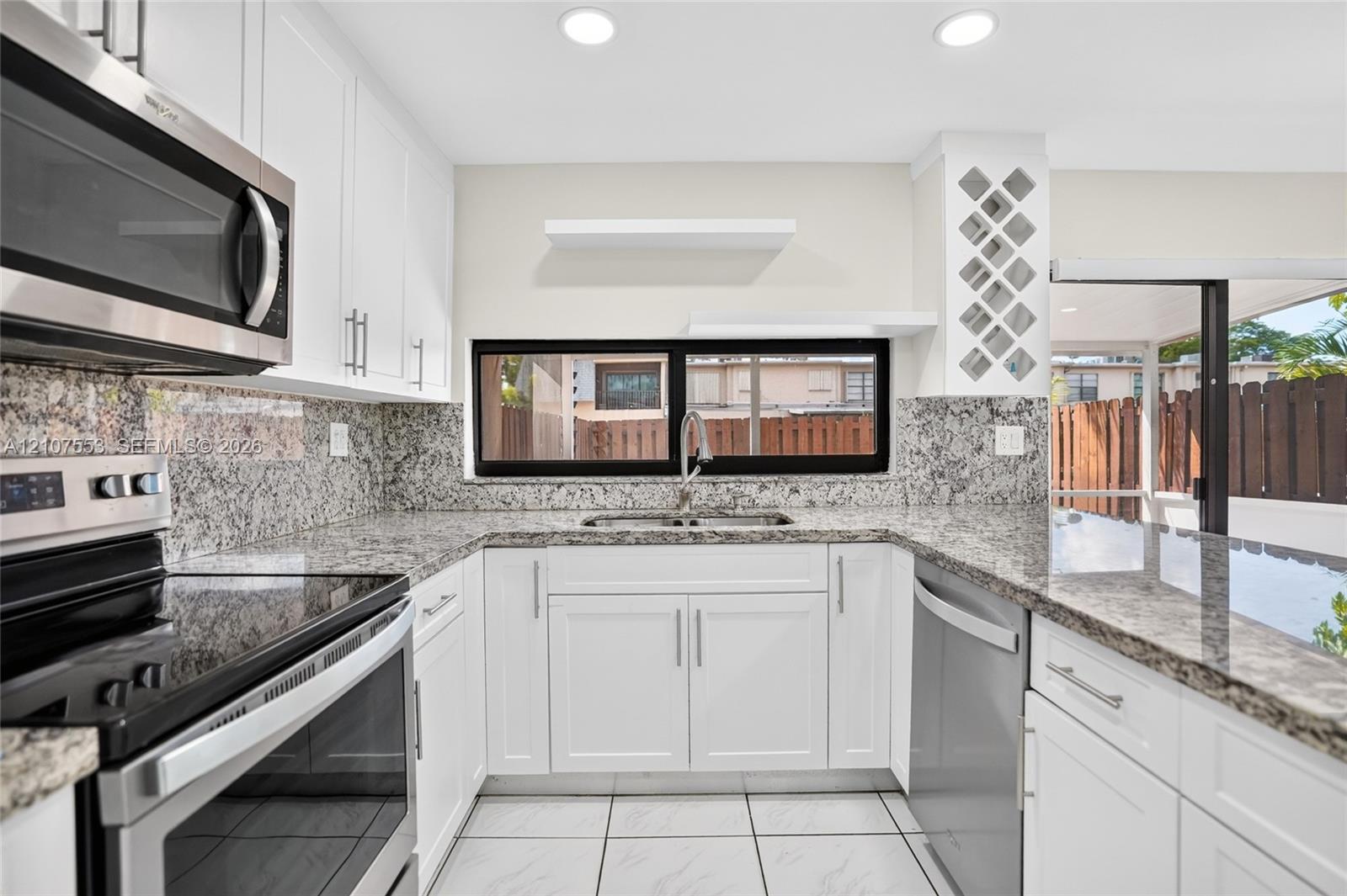 Kitchen featuring white shaker-style cabinetry, stone countertops with matching backsplash, built-in wine rack, stainless steel appliances, and tile flooring