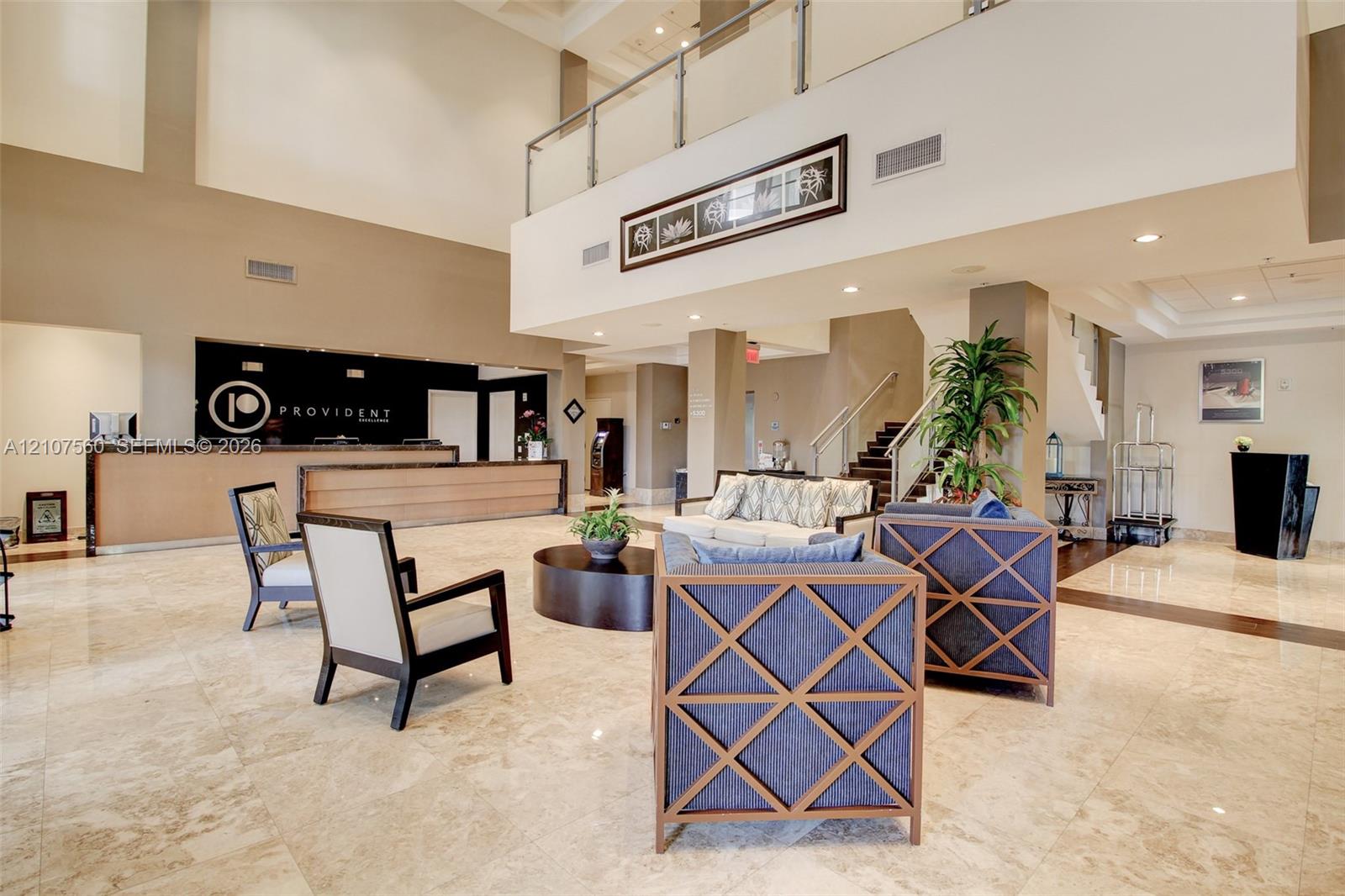 Expansive lobby featuring vaulted ceilings, polished stone flooring, a built-in reception desk, and a mezzanine level with glass and metal railings